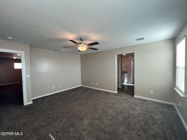 unfurnished room featuring visible vents, dark carpet, a textured ceiling, and baseboards