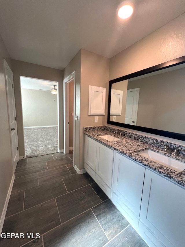 full bath featuring double vanity, wood finish floors, a sink, and baseboards