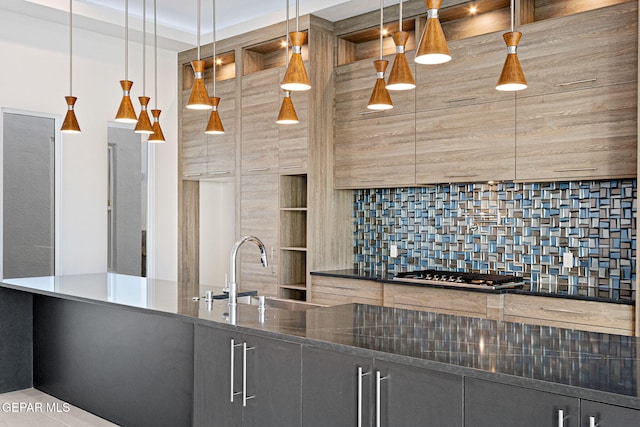 kitchen featuring a sink, stainless steel gas stovetop, backsplash, dark stone countertops, and pendant lighting