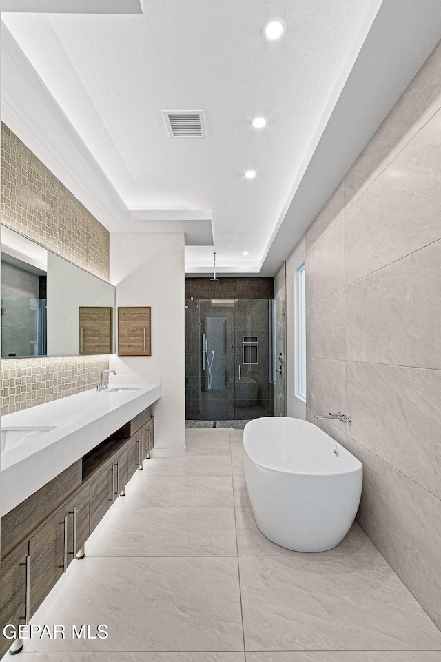 bathroom with double vanity, visible vents, a freestanding tub, a shower stall, and a sink