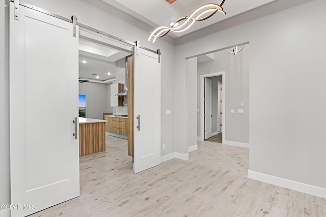 spare room with light wood-style floors, a barn door, baseboards, and an inviting chandelier