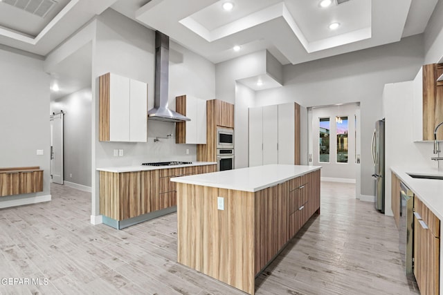 kitchen with a barn door, wall chimney exhaust hood, modern cabinets, appliances with stainless steel finishes, and a center island