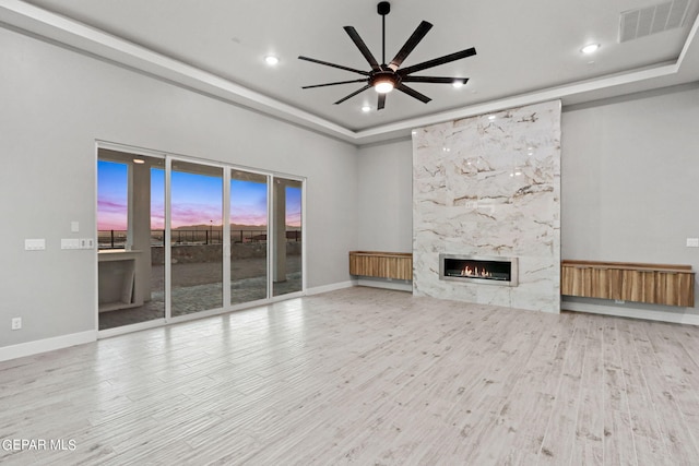 unfurnished living room featuring a premium fireplace, visible vents, a tray ceiling, and wood finished floors