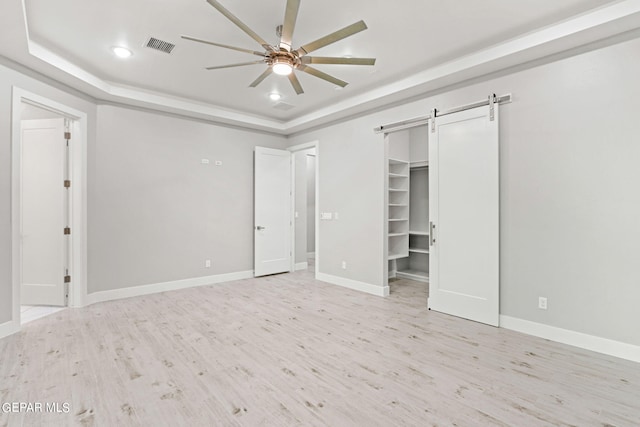 unfurnished bedroom featuring light wood-type flooring, a barn door, baseboards, and a raised ceiling