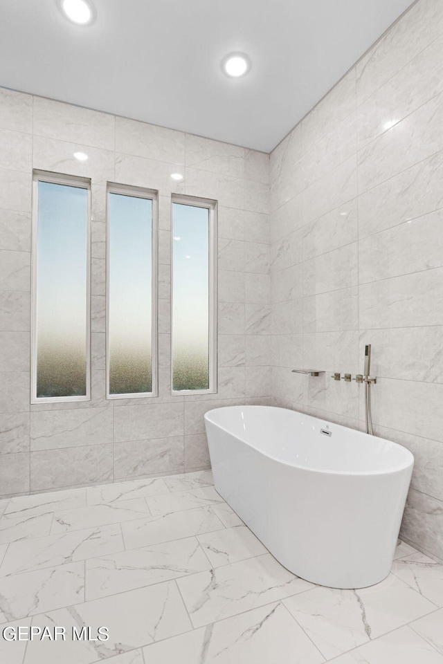 bathroom featuring marble finish floor and tile walls