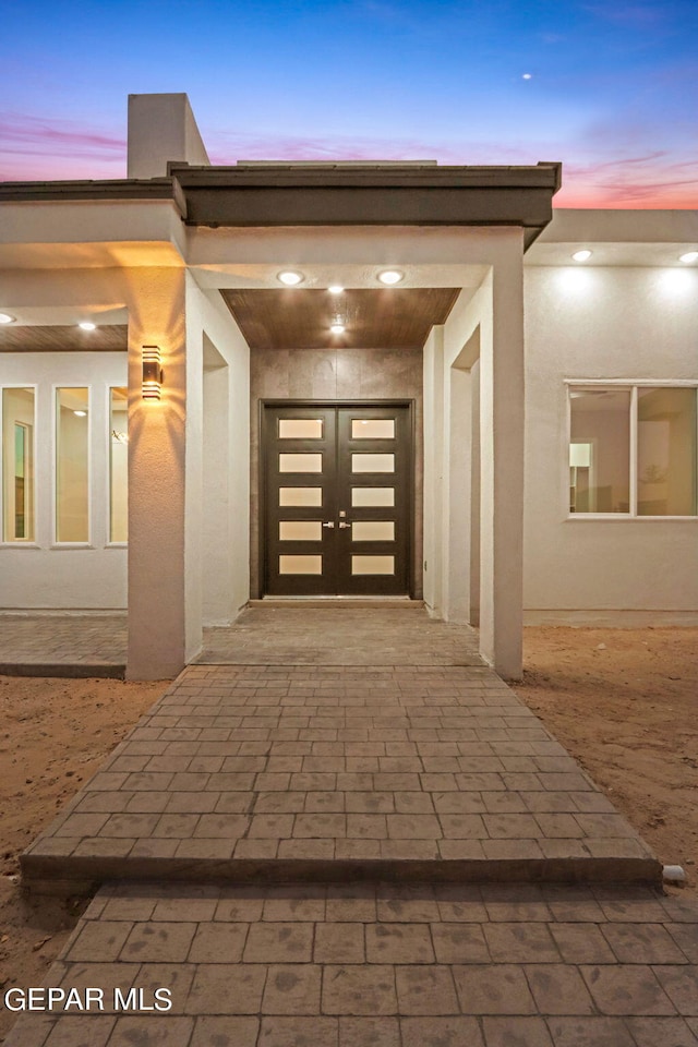 exterior entry at dusk with a garage, decorative driveway, and stucco siding