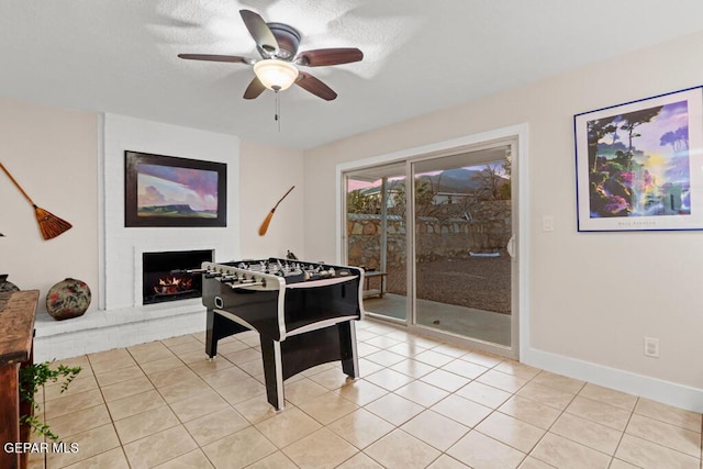 playroom featuring ceiling fan, a fireplace, baseboards, and light tile patterned floors