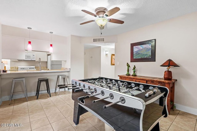 recreation room featuring a textured ceiling, visible vents, a ceiling fan, and light tile patterned flooring