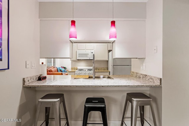 kitchen with a peninsula, white appliances, a sink, and white cabinetry