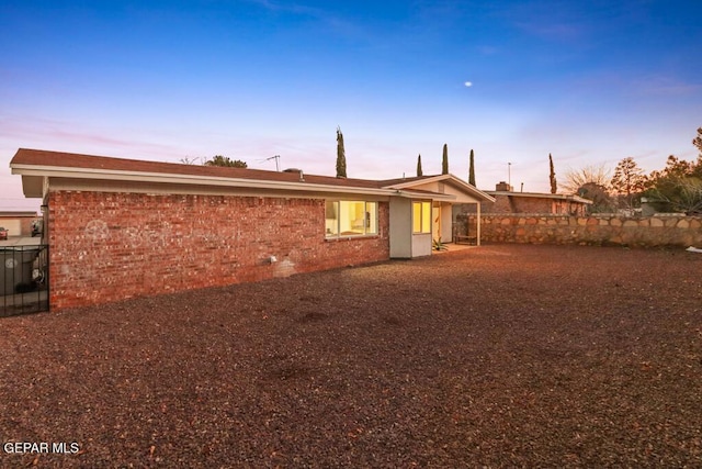 back of property at dusk featuring brick siding and fence