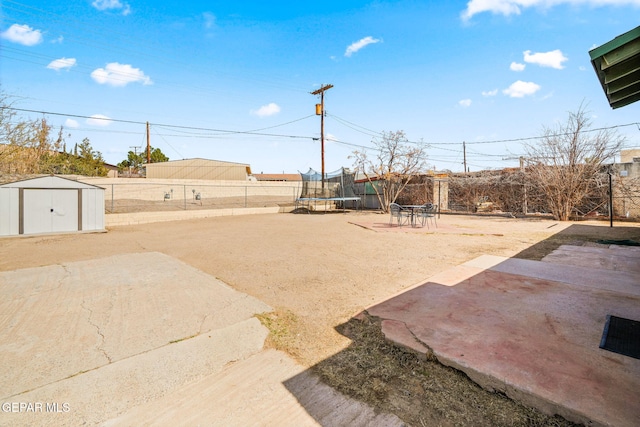 view of yard featuring a fenced backyard, an outbuilding, a trampoline, a storage unit, and a patio area