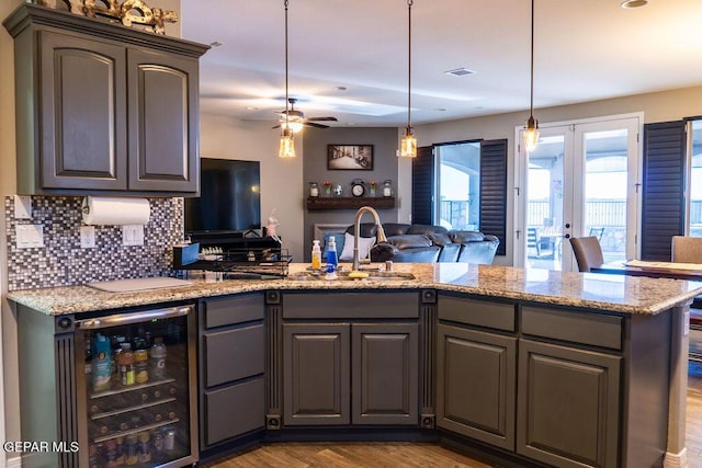 kitchen featuring tasteful backsplash, open floor plan, a sink, wood finished floors, and beverage cooler