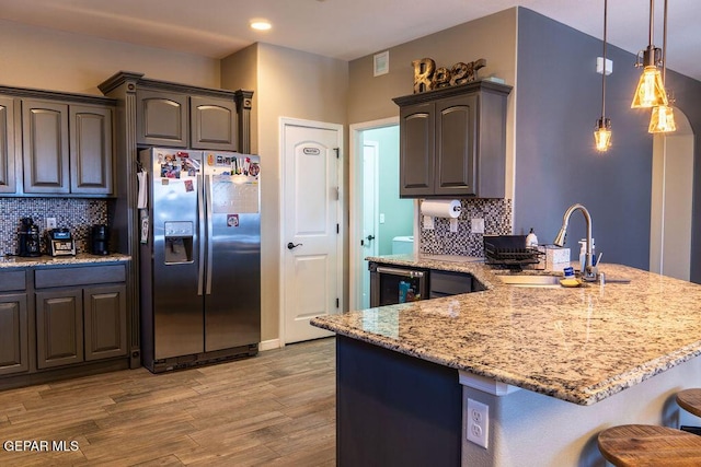 kitchen with light stone counters, a sink, wood finished floors, stainless steel fridge, and a peninsula