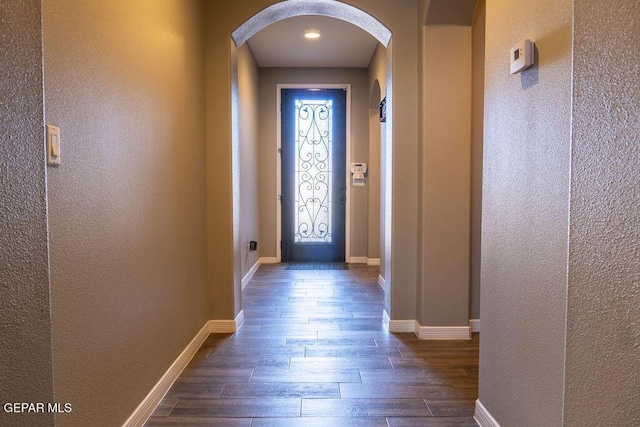 entryway featuring arched walkways, dark wood finished floors, and baseboards