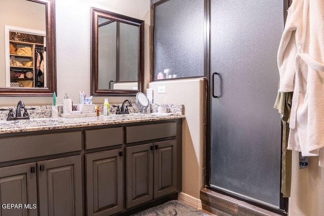 full bath featuring double vanity, a shower stall, a spacious closet, and a sink