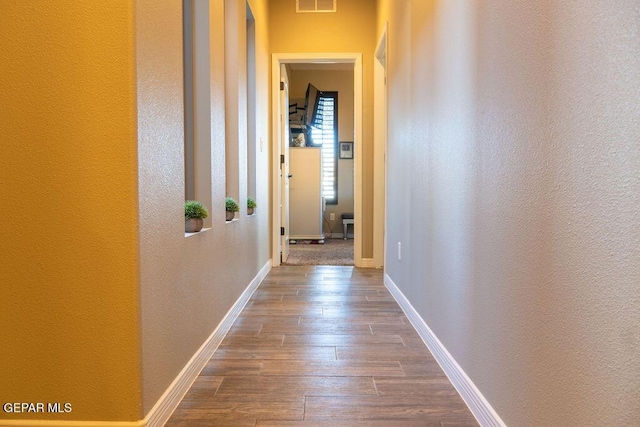 corridor with dark wood-style floors, baseboards, and visible vents