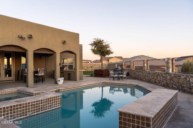 pool at dusk featuring a patio, fence, a fenced in pool, and an in ground hot tub