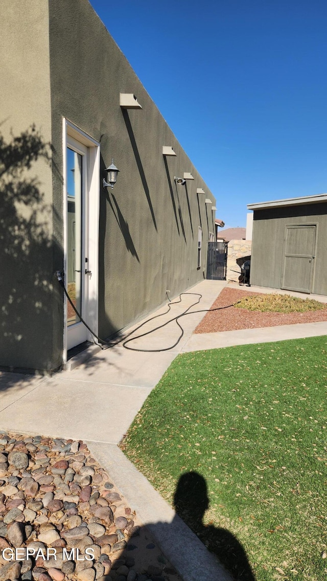 view of side of home featuring a storage unit, an outdoor structure, a lawn, and stucco siding