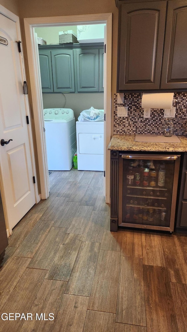 clothes washing area with wine cooler, washing machine and dryer, cabinet space, and wood finished floors