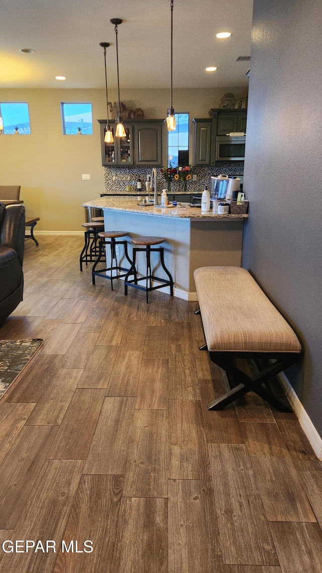 kitchen featuring a breakfast bar area, baseboards, decorative backsplash, stainless steel microwave, and dark wood finished floors