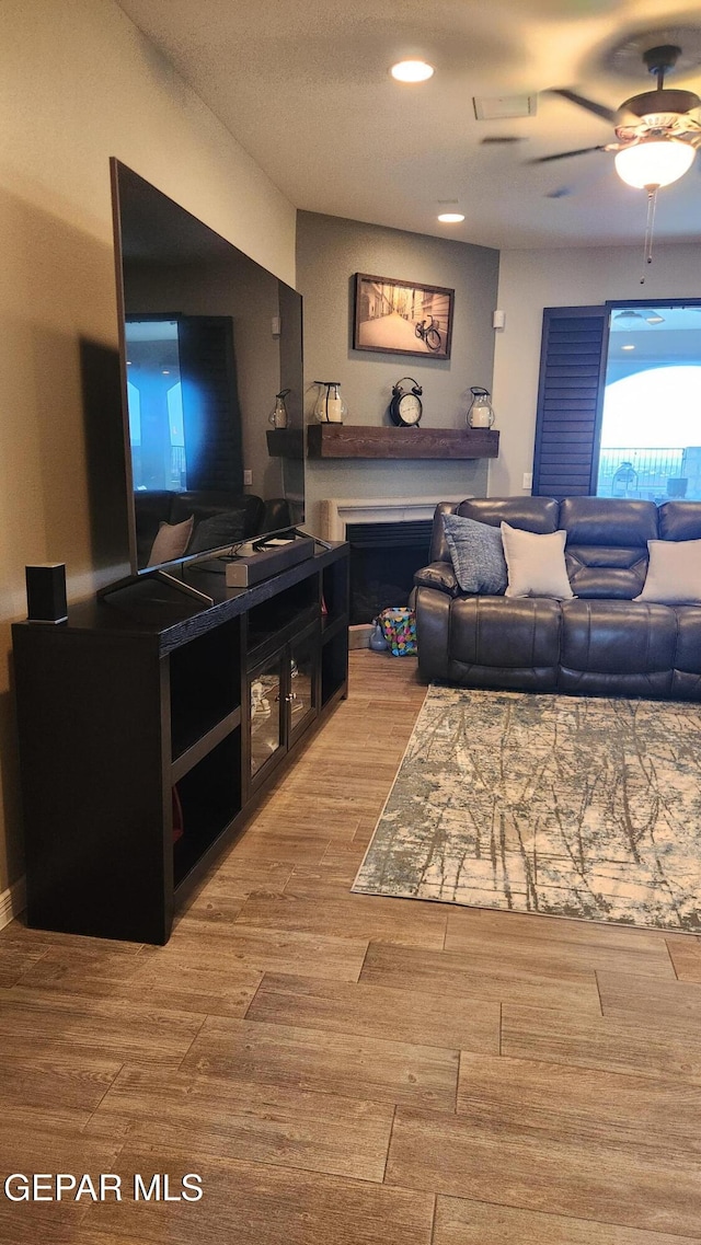 living area featuring a fireplace, wood finished floors, and a ceiling fan