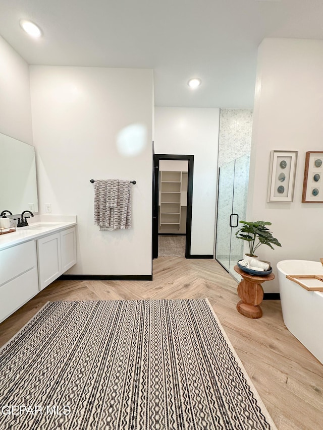 full bathroom with a stall shower, wood finished floors, vanity, a freestanding tub, and recessed lighting