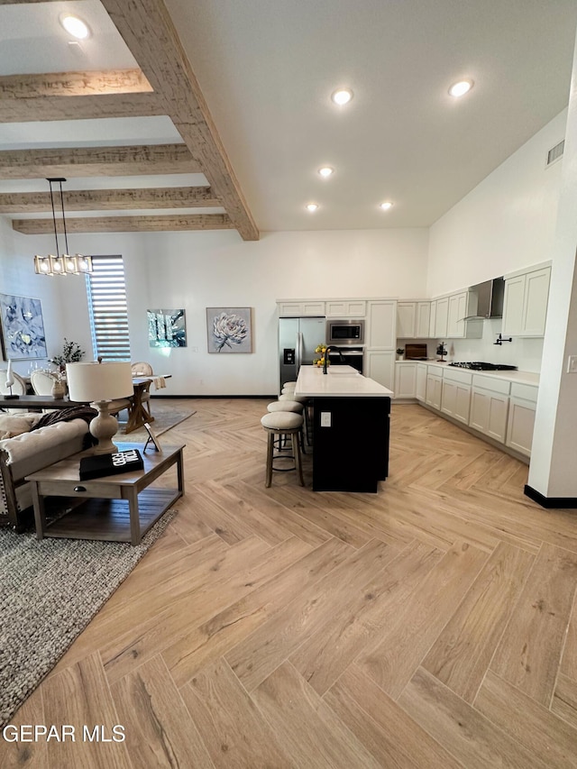 kitchen featuring stainless steel appliances, visible vents, a kitchen island with sink, wall chimney range hood, and beamed ceiling