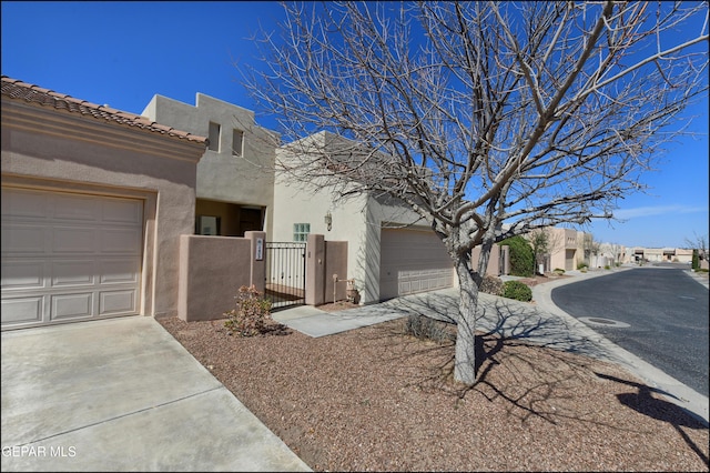 view of front of house featuring a gate, a tiled roof, concrete driveway, and stucco siding