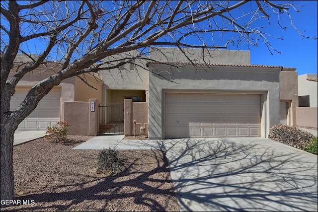 adobe home with a gate, driveway, and stucco siding