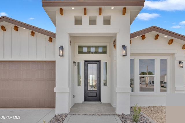 doorway to property with an attached garage, board and batten siding, and stucco siding