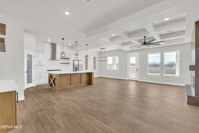 kitchen with tasteful backsplash, light countertops, light wood-style flooring, open floor plan, and wall chimney exhaust hood