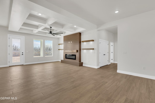 unfurnished living room featuring a large fireplace, coffered ceiling, wood finished floors, and baseboards