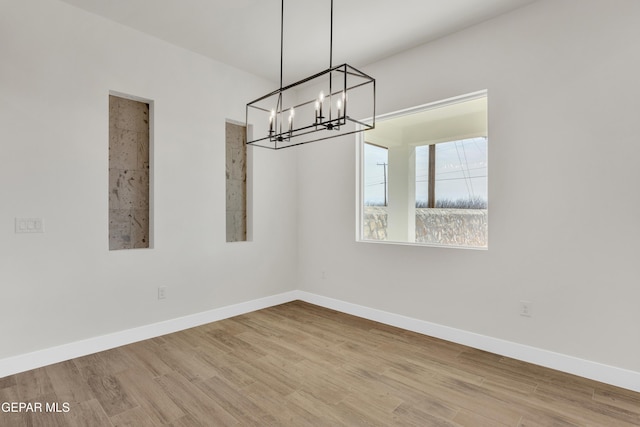 unfurnished dining area with a notable chandelier, baseboards, and wood finished floors