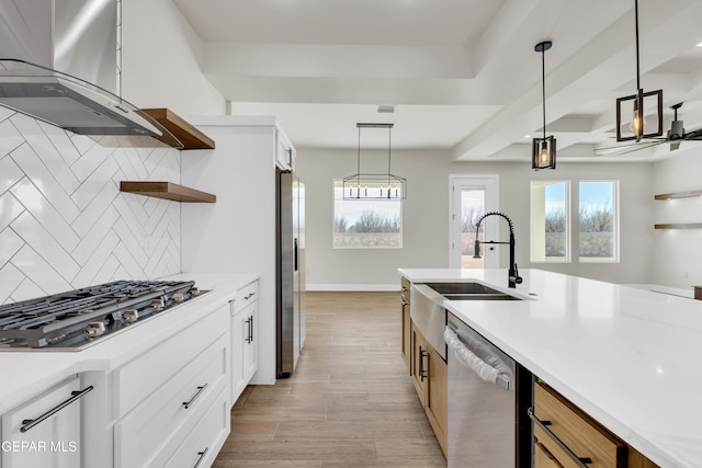 kitchen featuring stainless steel appliances, light countertops, wall chimney range hood, open shelves, and a sink