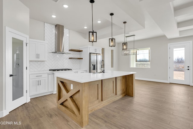 kitchen featuring stainless steel refrigerator with ice dispenser, light wood finished floors, open shelves, light countertops, and wall chimney range hood