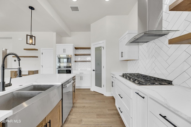 kitchen with visible vents, stainless steel appliances, wall chimney range hood, open shelves, and a sink