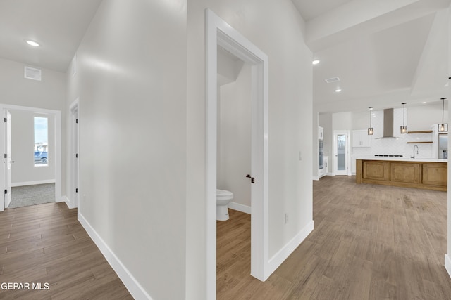 hall featuring light wood-type flooring, visible vents, baseboards, and recessed lighting