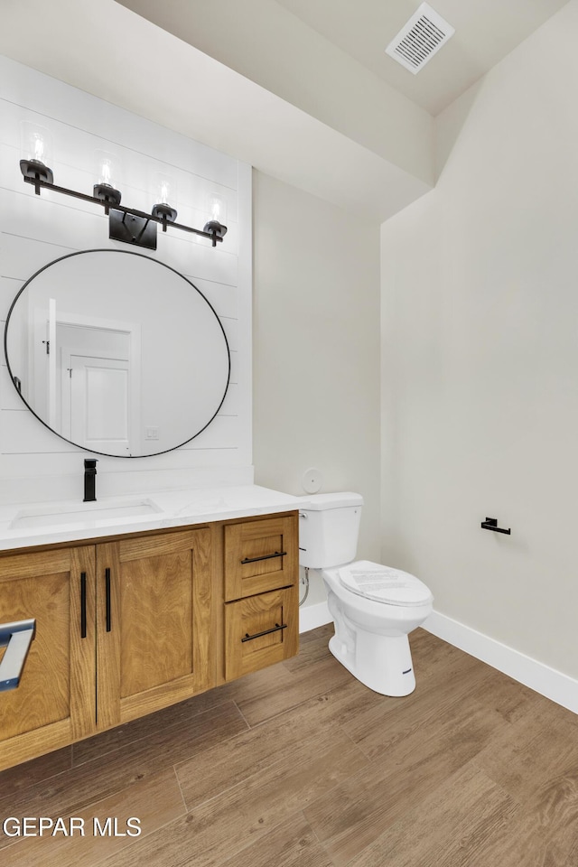 bathroom with toilet, vanity, wood finished floors, and visible vents