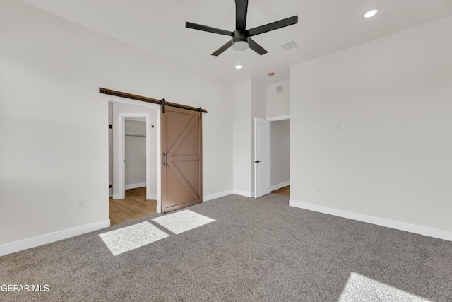 unfurnished bedroom featuring a barn door, visible vents, baseboards, carpet floors, and recessed lighting