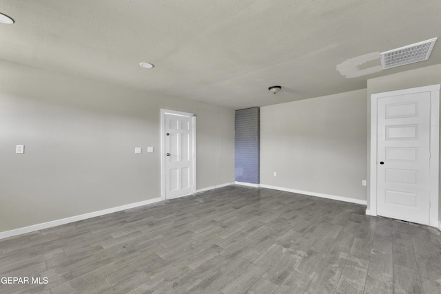 empty room with visible vents, a textured ceiling, baseboards, and wood finished floors