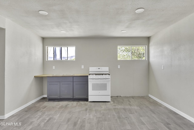 kitchen with baseboards, light wood finished floors, gray cabinetry, and white gas range