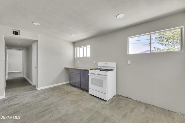 kitchen with a textured ceiling, baseboards, light wood-style floors, white gas range oven, and gray cabinets