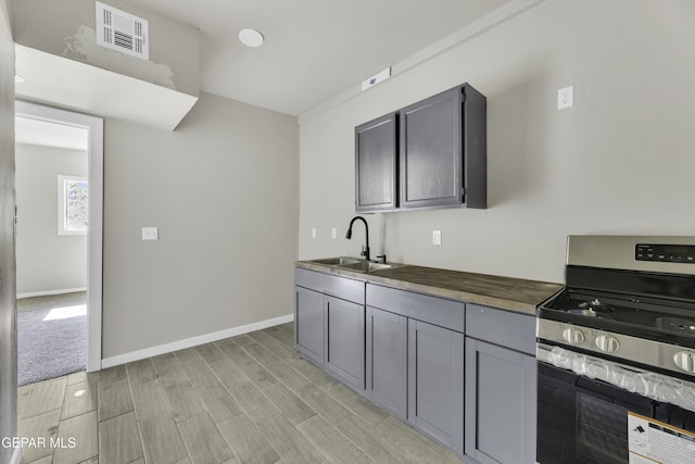 kitchen featuring visible vents, gray cabinetry, a sink, gas range, and baseboards