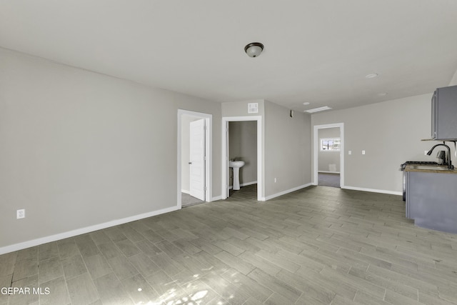 unfurnished living room with a sink, wood finished floors, visible vents, and baseboards