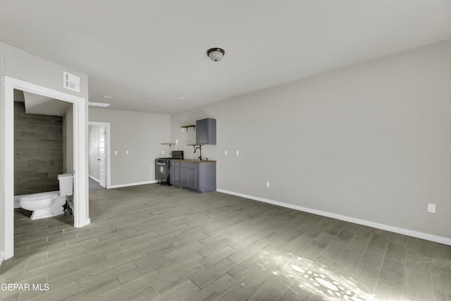 unfurnished living room with visible vents, a sink, baseboards, and wood finished floors