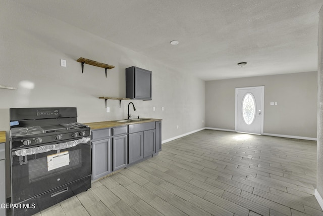 kitchen with open shelves, baseboards, black gas stove, wooden counters, and a sink