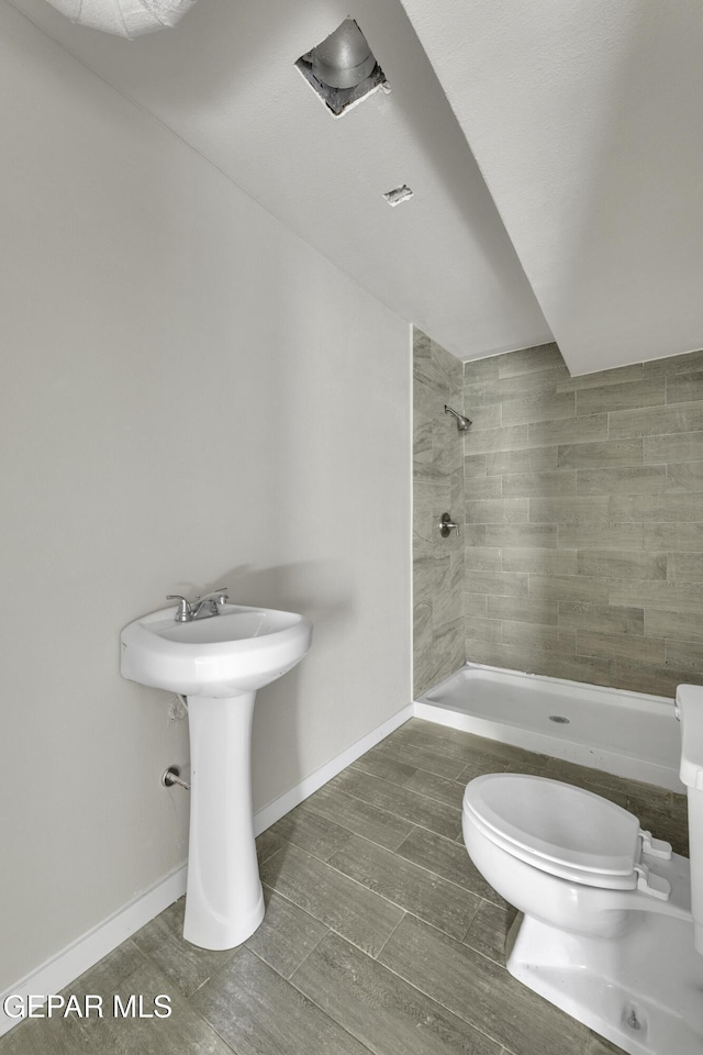 bathroom featuring tiled shower, toilet, and baseboards