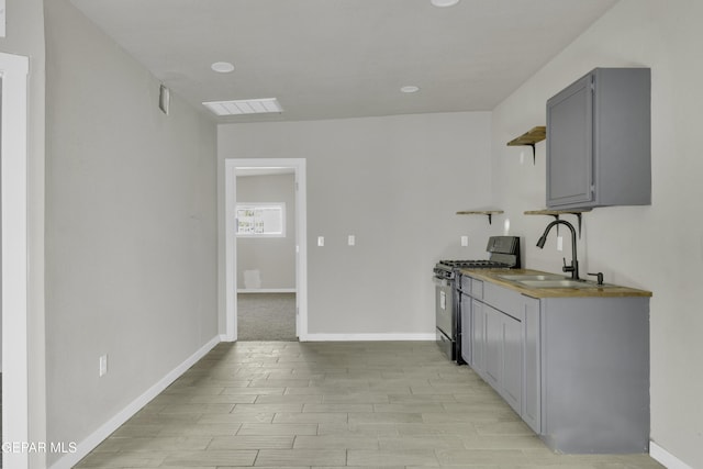 kitchen featuring stainless steel gas range oven, a sink, visible vents, gray cabinets, and open shelves