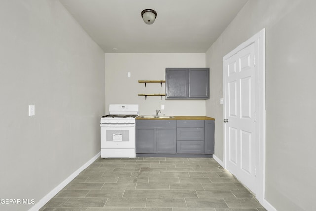 kitchen featuring open shelves, gray cabinets, a sink, baseboards, and white gas range oven