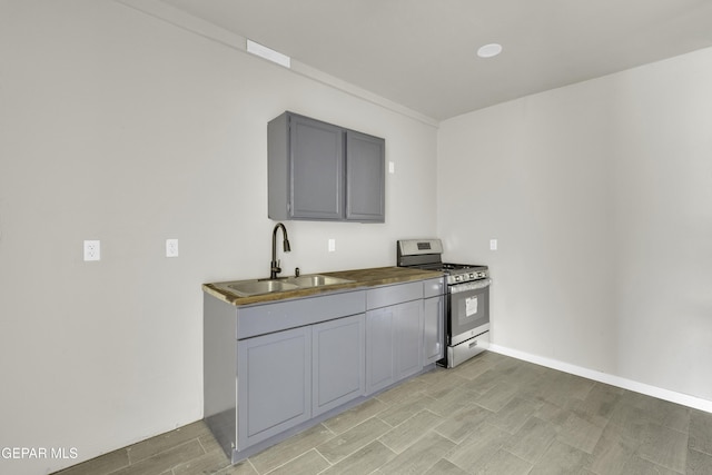 kitchen featuring wood finish floors, gray cabinetry, a sink, stainless steel gas range oven, and baseboards